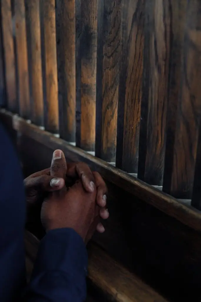 Close-up of clasped hands in a wooden confessional, evoking prayer and reflection.